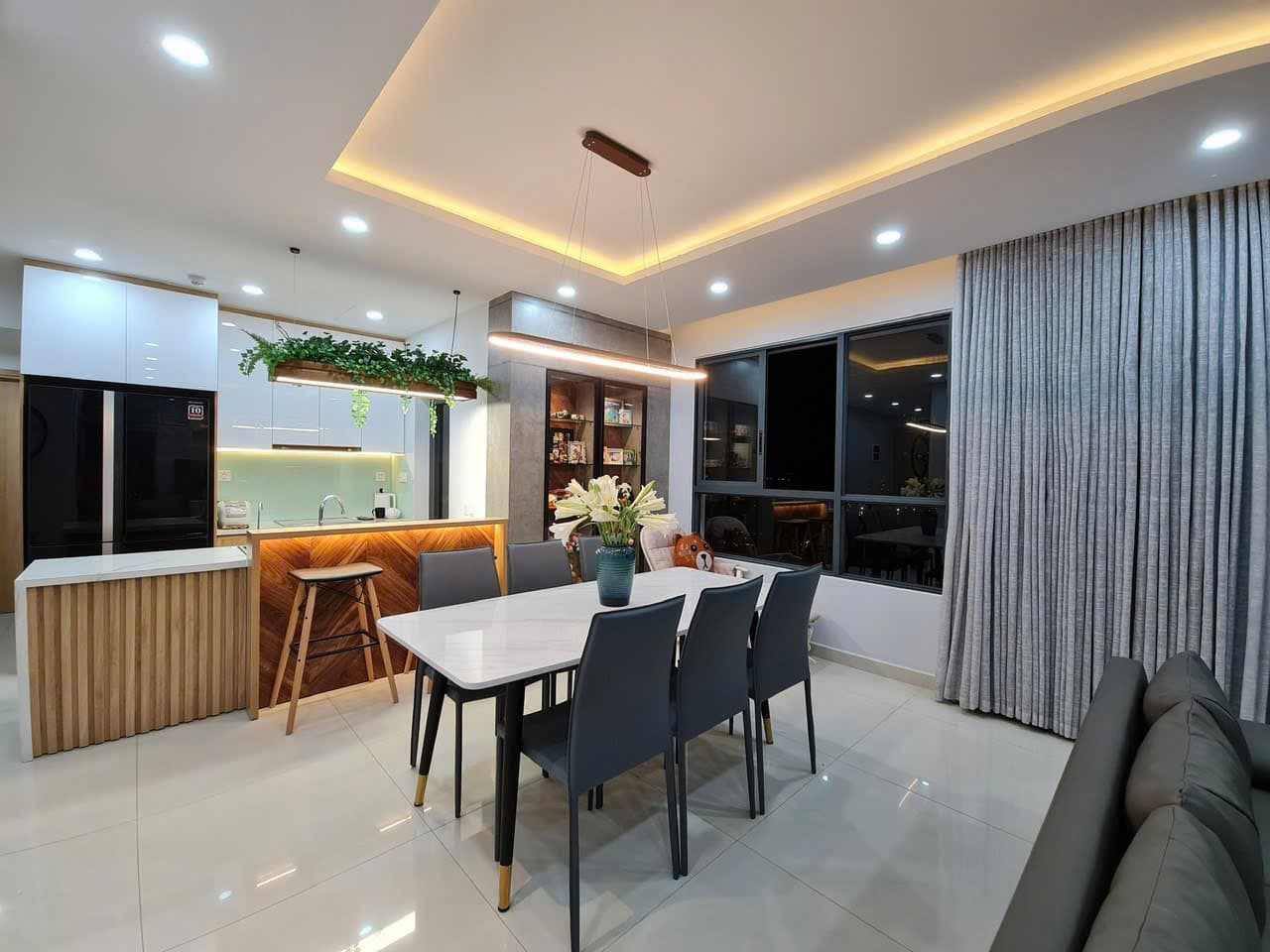 Không gian bếp hiện đại liền bàn ăn với quầy bar ốp gỗ và hệ tủ bếp sáng màu