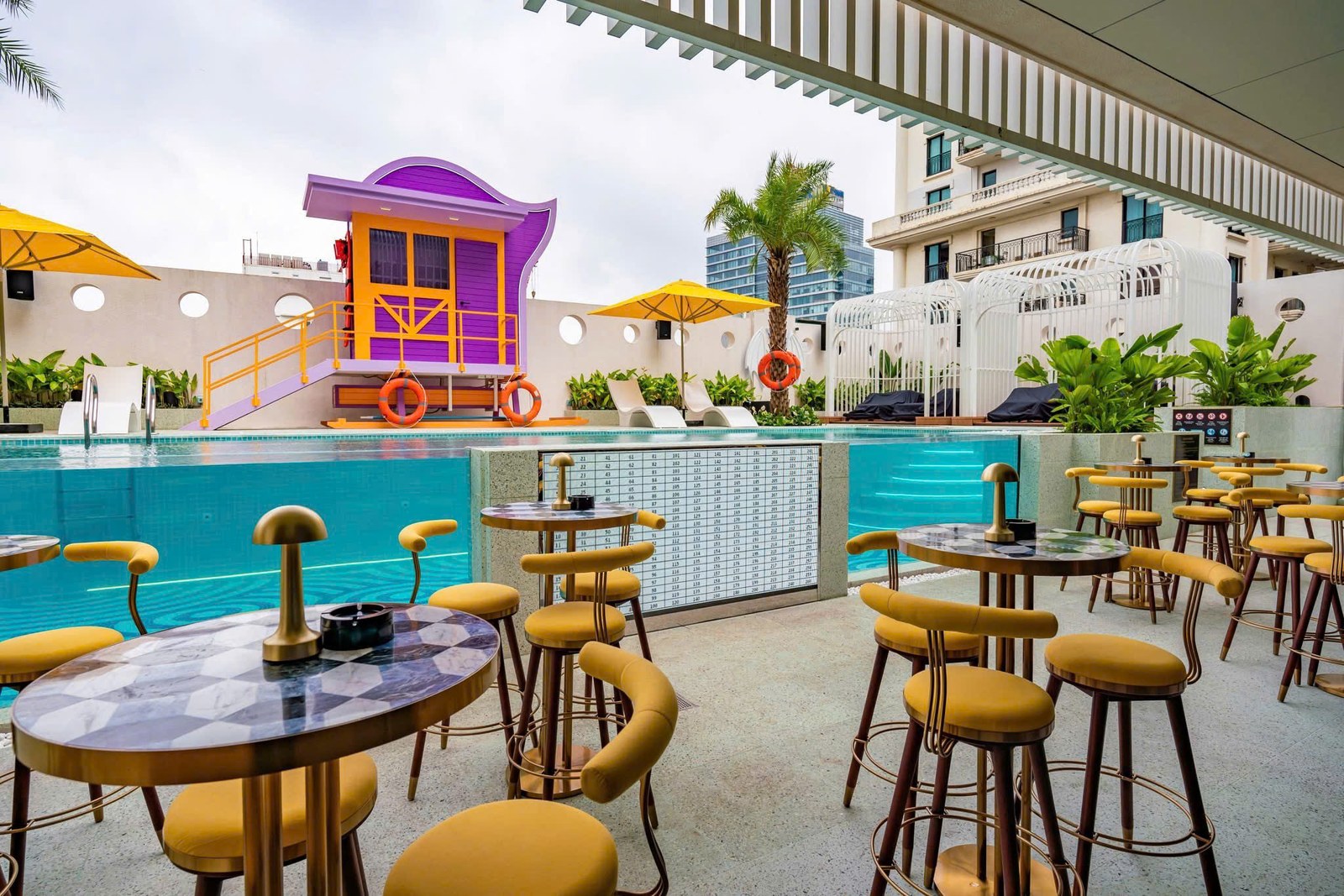 Quầy bar cạnh hồ bơi trong khách sạn Movenpick với ghế cao, bàn tròn và tông vàng nổi bật